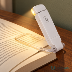 White rechargeable folding book light clipped to an open book on a timber bedside table.