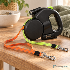 Black dual retractable dog lead on a timber table with orange and neon green leads and metal clips.
