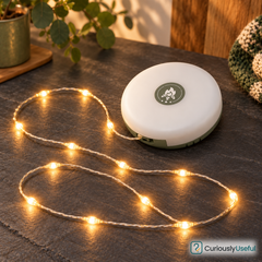 White circular rechargeable camping light reel with warm string lights visible on a stone surface.