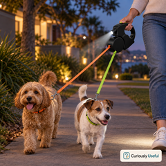 Two dogs walking at dusk with the black dual retractable dog lead and built-in LED light switched on.