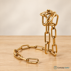 Gold floating chain wine bottle holder without a bottle on a pale timber surface.